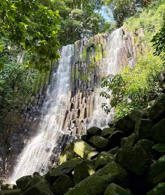 Waterfall in Suchitoto, El Salvador with lush greenery and basalt rock formations.