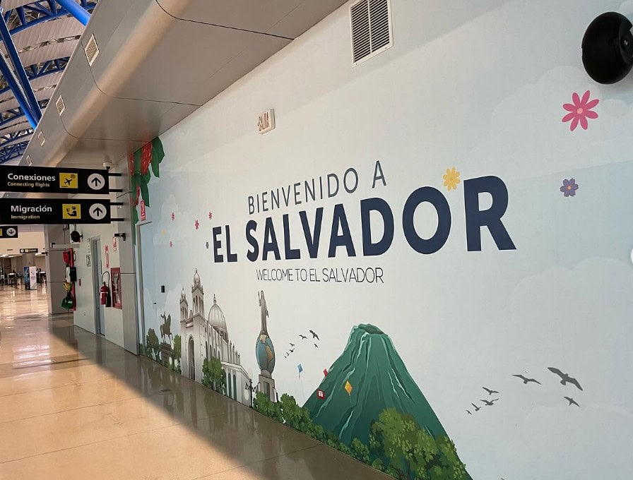 Airport wall mural welcoming visitors to El Salvador with iconic landmarks and natural scenery.