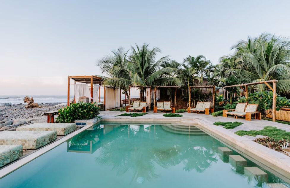 Luxurious beachfront pool with cabanas and palm trees in El Salvador.